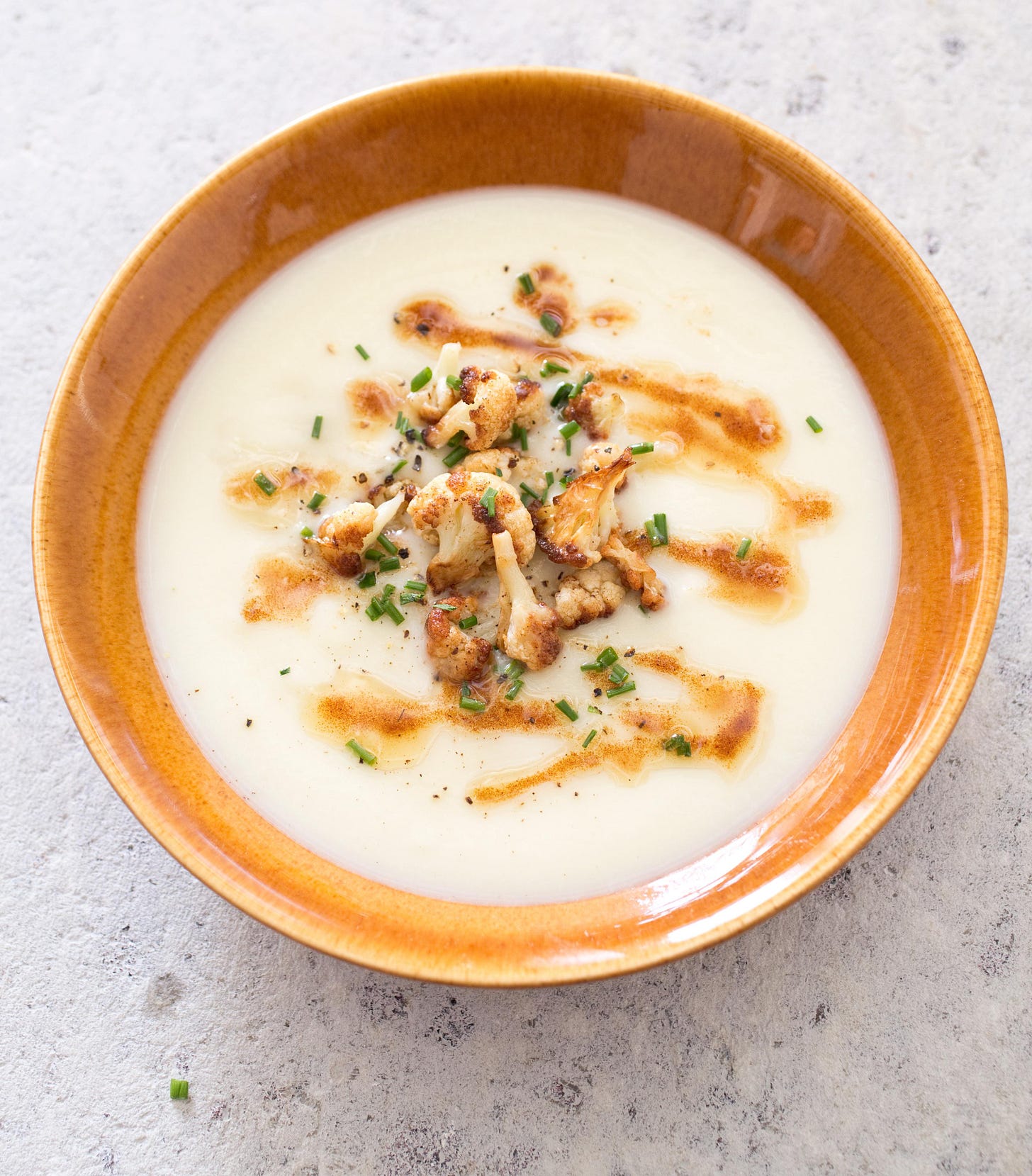 brown bowl of cauliflower soup with roasted cauliflower garnish