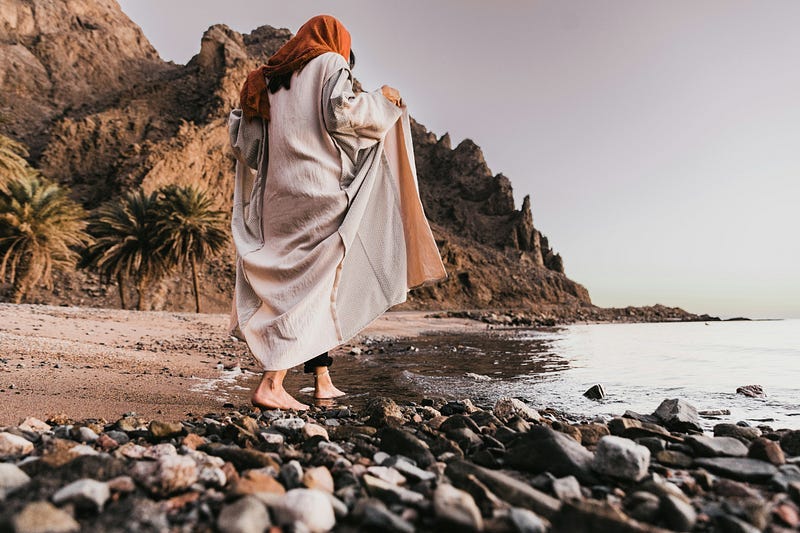 Woman walking on the beach with long robes and a headscarf