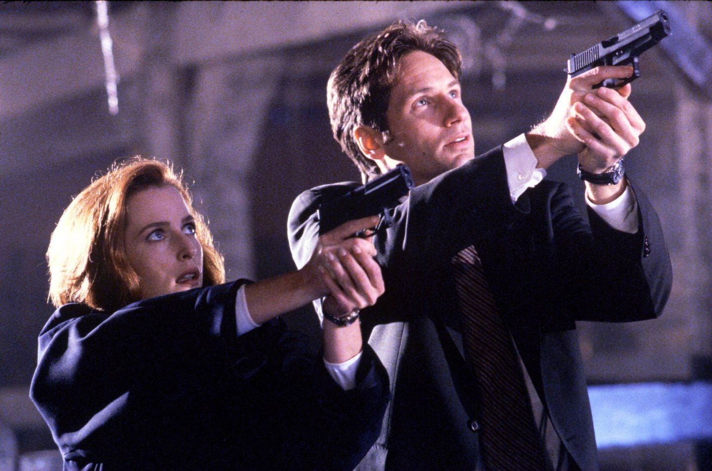 A man and woman hold guns with two hands, one hand around the grip and the other supporting it from below