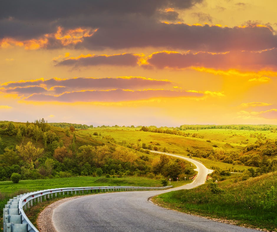 Paved road winding through a grassy valley with a cloudy golden sky