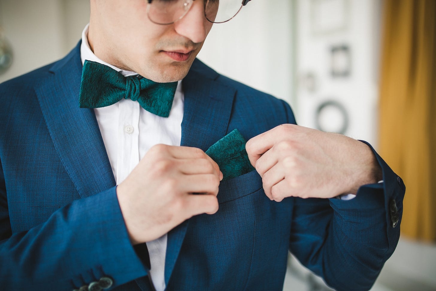 A young man in a suit fixes his pocket square.