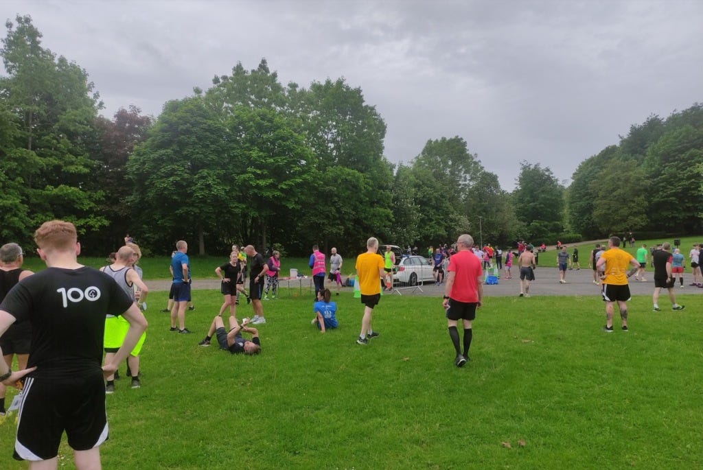 People stand around, with a couple lying down, at the finish area which is on a large grassy spot with paths round the edge for the actual running.