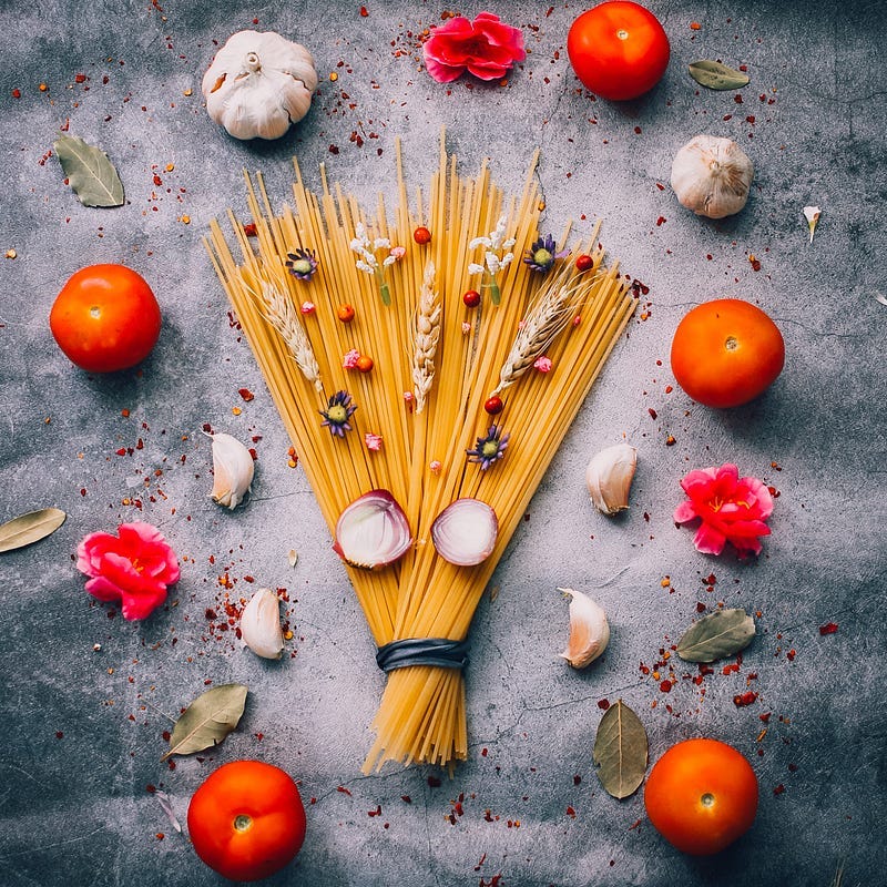 A fan of spaghetti displayed with red tomatoes and cloves of garlic
