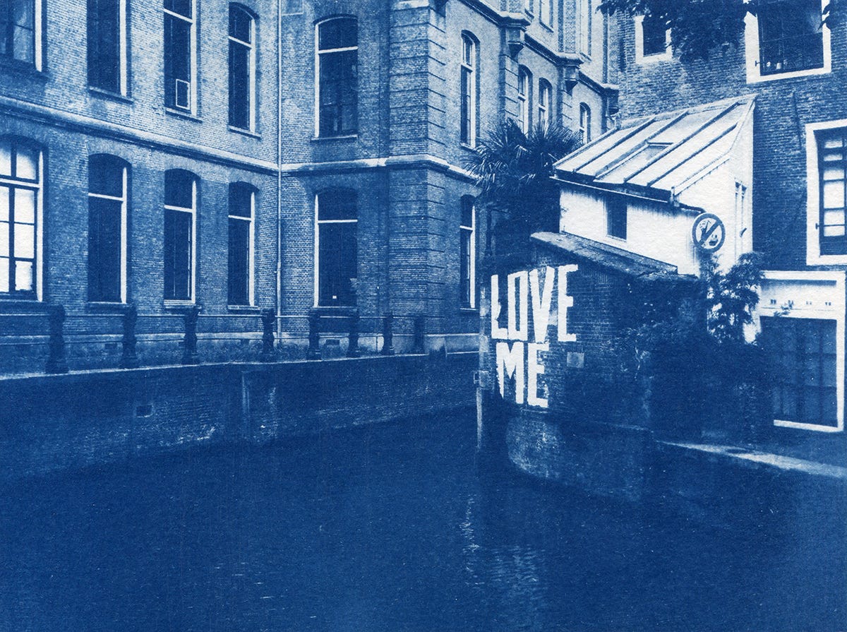 Vieil immeuble à Amsterdam avec un canal qui passe à ses pieds et un graffiti "Love Me" sur un mur en briques.