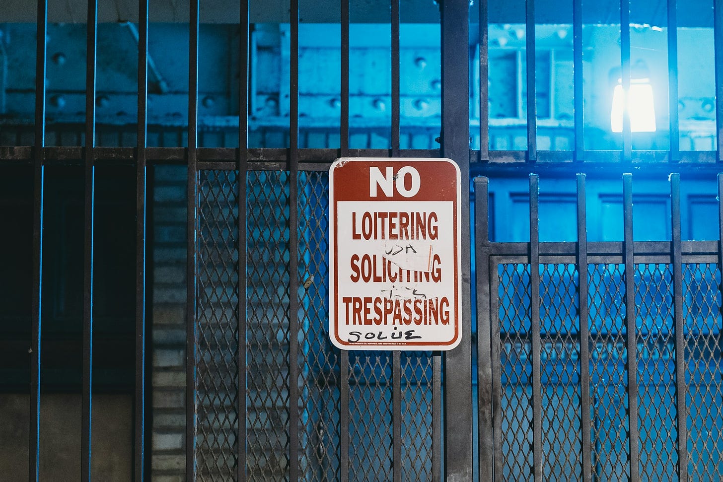 a sign on a metal fence No Loitering, No Soliciting, No Trespassing
