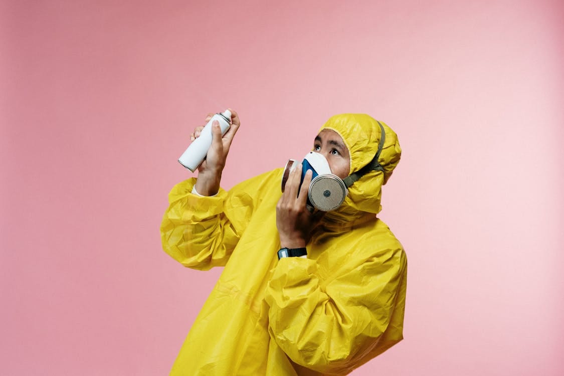 Free Man wearing a yellow protective suit and respirator, holding a spray can against a pink background. Stock Photo