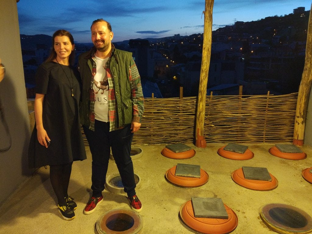 Zura and his wife stand in their Marani, with Tbilisi's night sky in the background