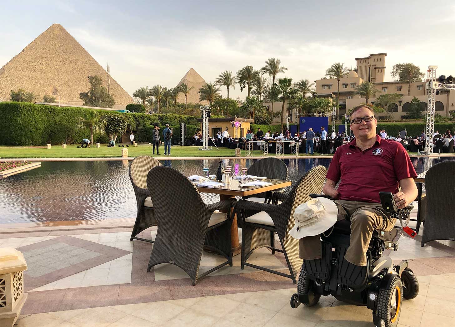 John seated in front of his power wheelchair in front of the Egyptian pyramids.