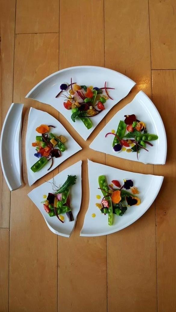 A colorful mix of vegetables is set out on a white plate that's broken into 5 large shards, with each shard containing a piles of vegetables artfully arranged. 