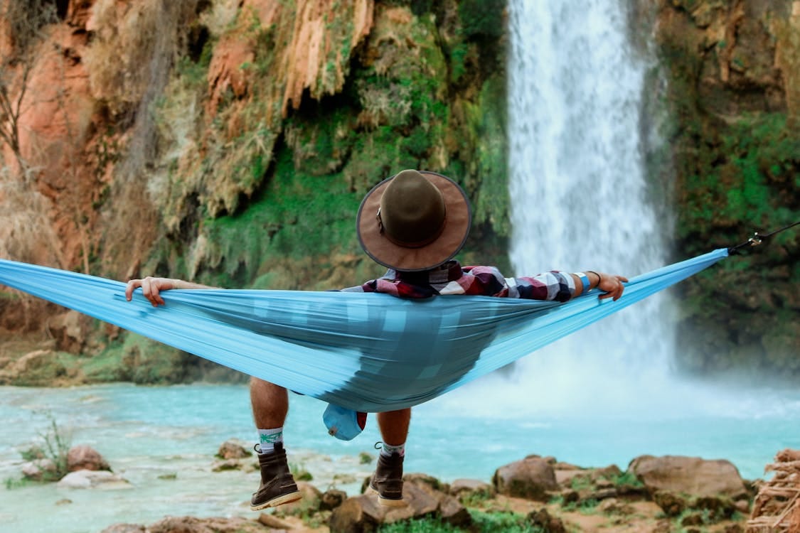 Free A person relaxes in a hammock by a waterfall, capturing the essence of tranquil outdoor leisure. Stock Photo