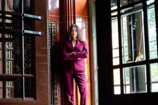 Deborah Gist, a red pantsuit, stands in front inside a school, with her arms crossed.