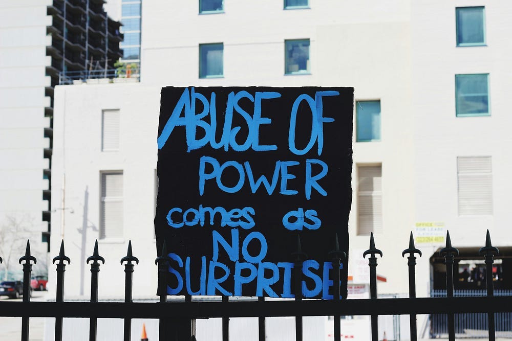 A painted sign, blue words on a black background. It reads: Abuse of power comes as no surprise. A painted sign, blue words on a black background. It reads: Abuse of power comes as no surprise.
