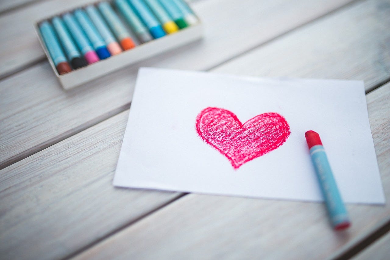 a drawing of a heart on a piece of paper surrounded by pastel crayons