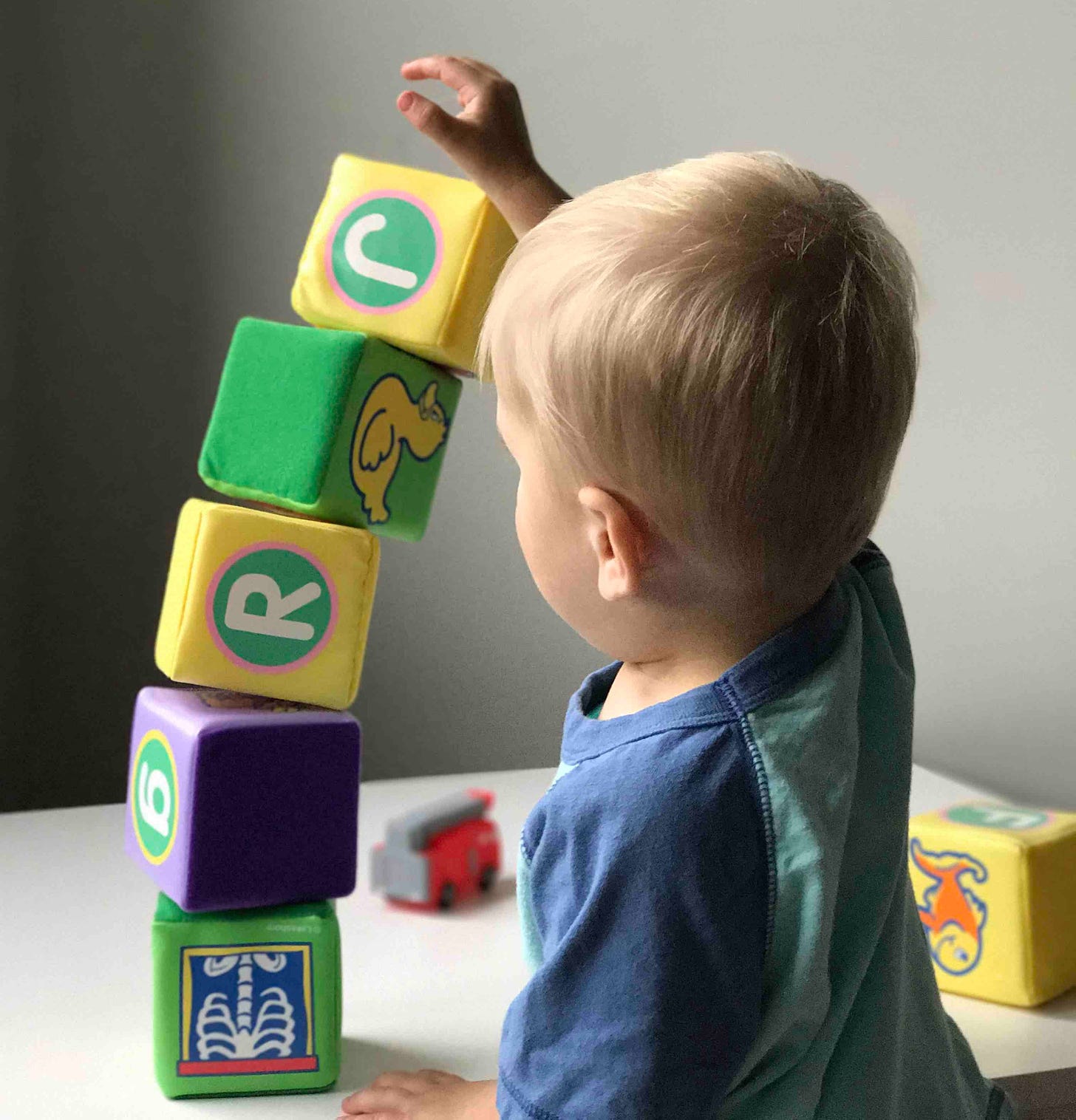 An infant stacking yellow, green and purple building blocks on top of eachother