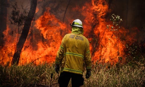 A firefighter stands in front of a controlled burn in bushland