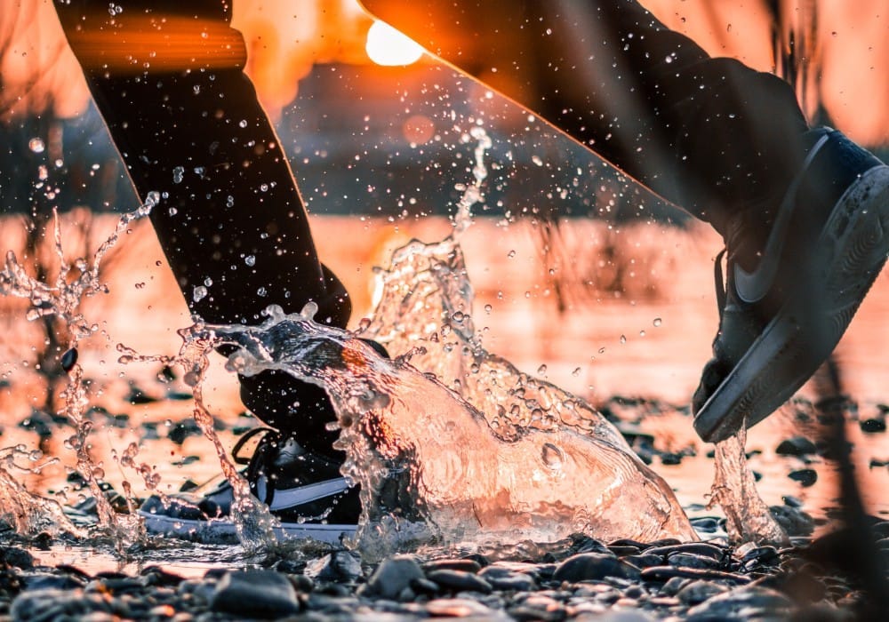 Man in Nike shoes splashing through puddle with orange sun setting
