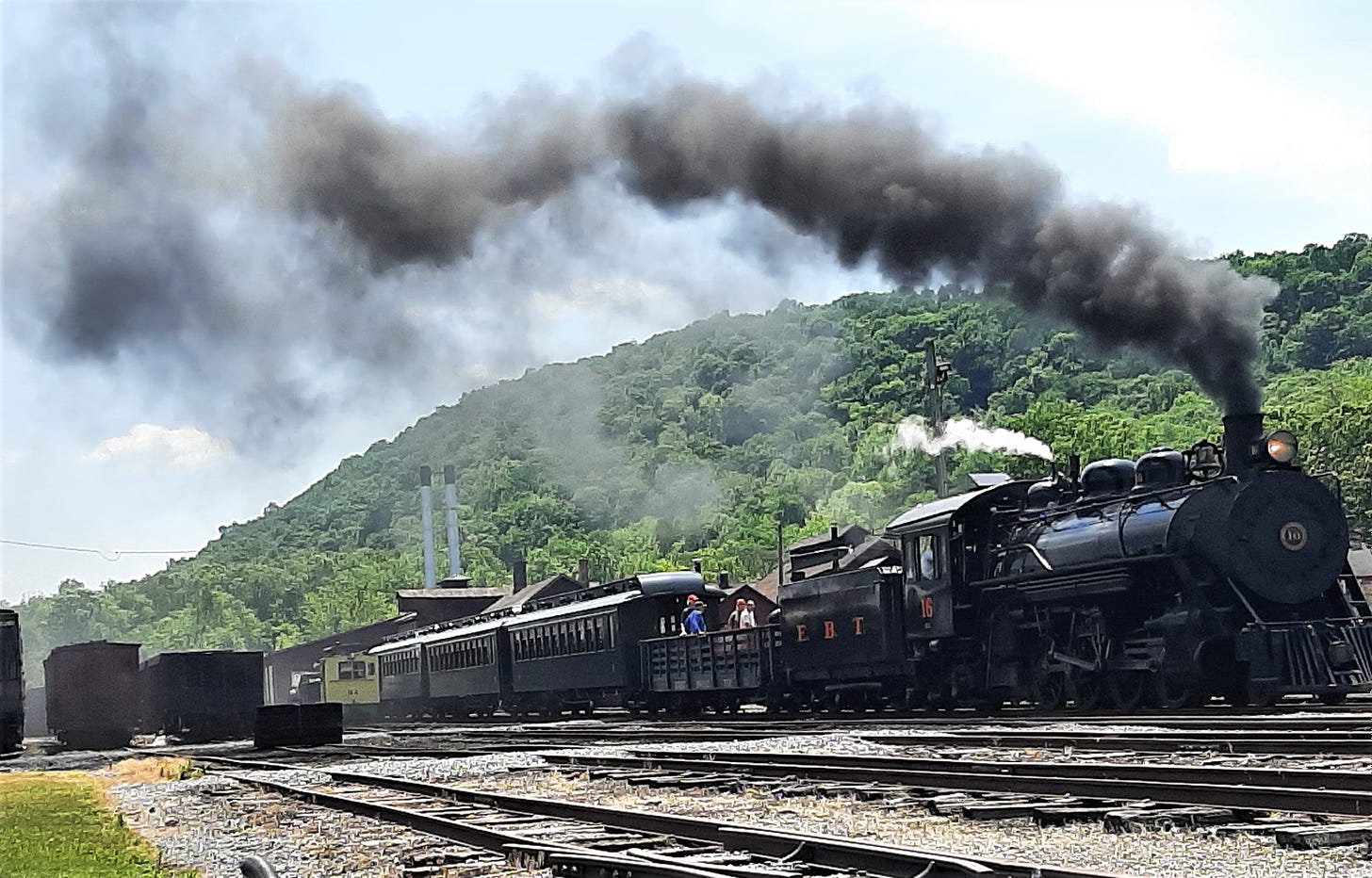 Black steam engine with black smoke pouring out, pulling train cars.