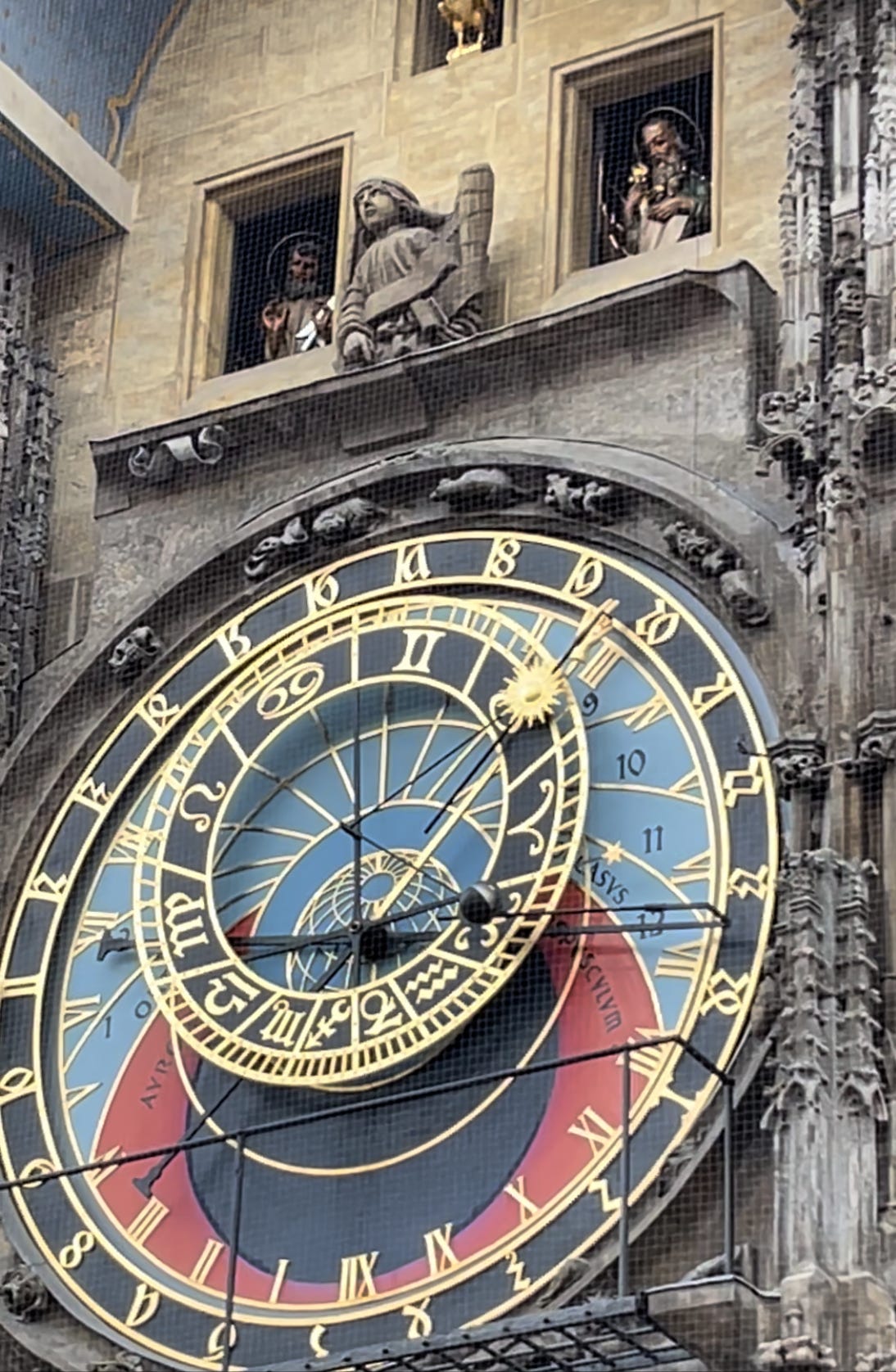 A clock of colorful dials calibrating the position of the sun and moon with astronomical details and above is windows with statues of various Catholic saints.