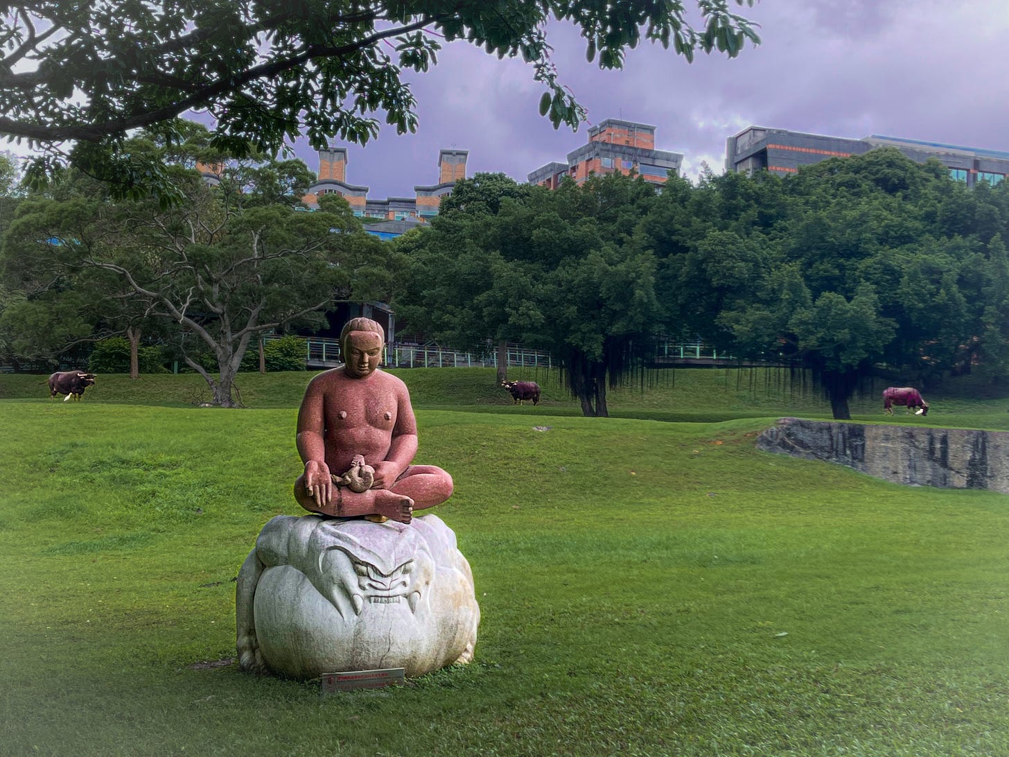 Three water buffalo graze behind a large Buddha statue at Taipei National University of the Arts