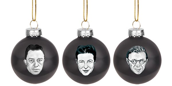 Three black glass ornaments featuring portraits of famous existentialist philosophers hanging above a product box labeled "Existentialist Ornaments". The ornaments display monochrome images of three individuals on dark spheres, suspended by gold strings.