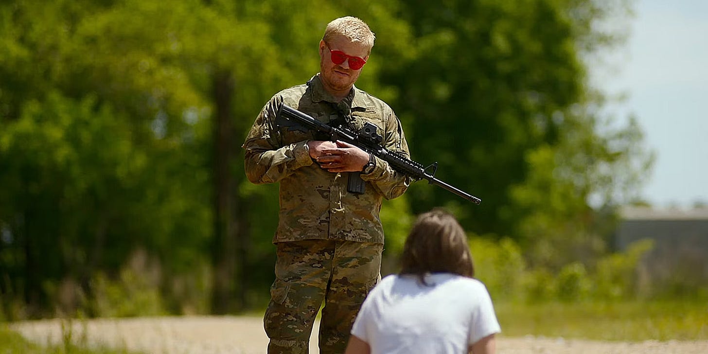 Alt text: "A resistance soldier stands guard over a young press reporter who is on her knees on the ground, depicting a tense moment of confrontation in the film.