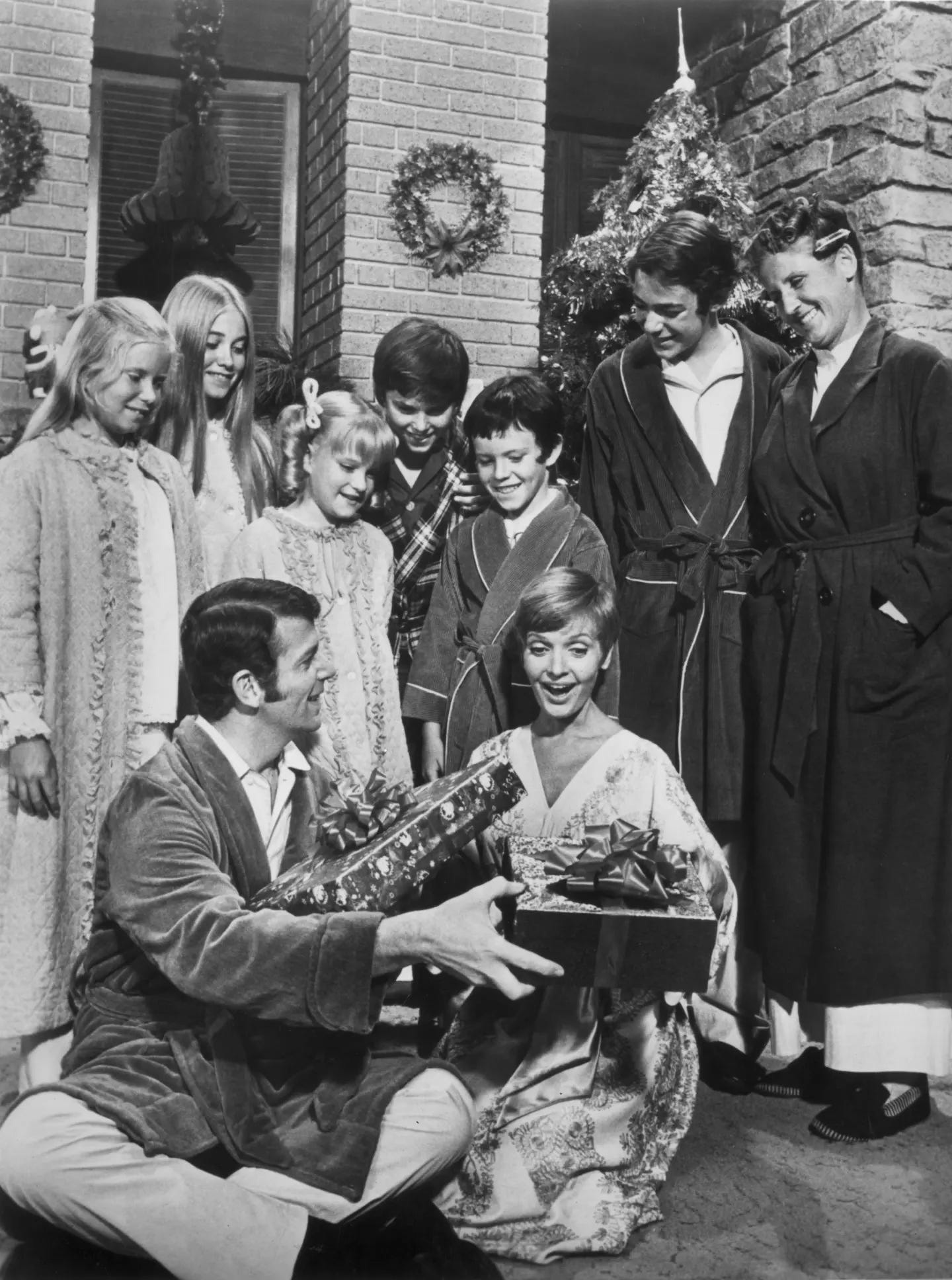 A black and white photo of the Brady family in pjs at Christmas opening gifts.