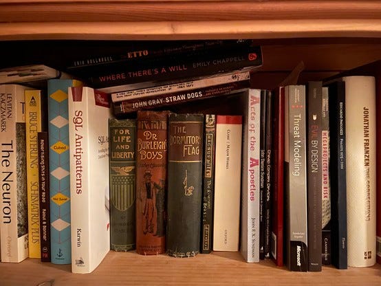 Photo of some jumbled books on a bookshelf, including my books The Pains, Cheap Complex Devices and Acts of the Apostles.