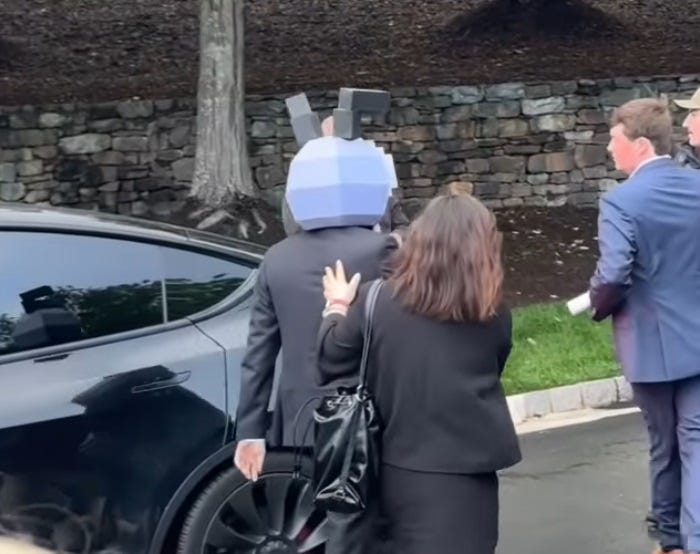 A man wearing an odd grey mask that covers his entire head is escorted by a woman into the property where Trump's crypto dinner took place. The front of the mask is not visible in the video. 