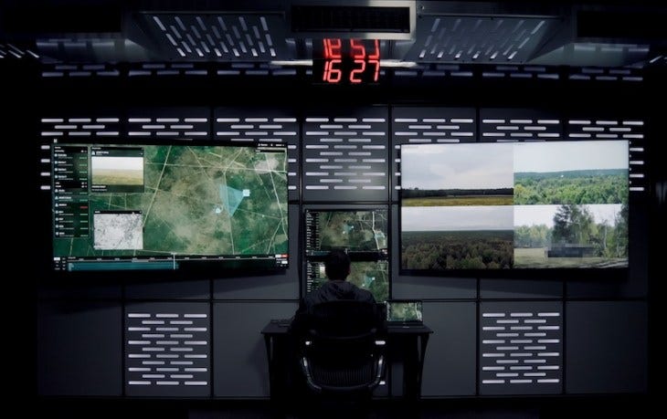 man sitting in front of two large video screens (defense tech)