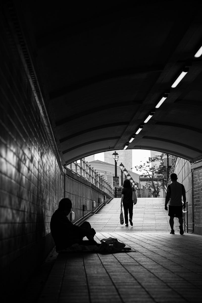 Black and white photo of a homeless man sitting in an underground tunnel.