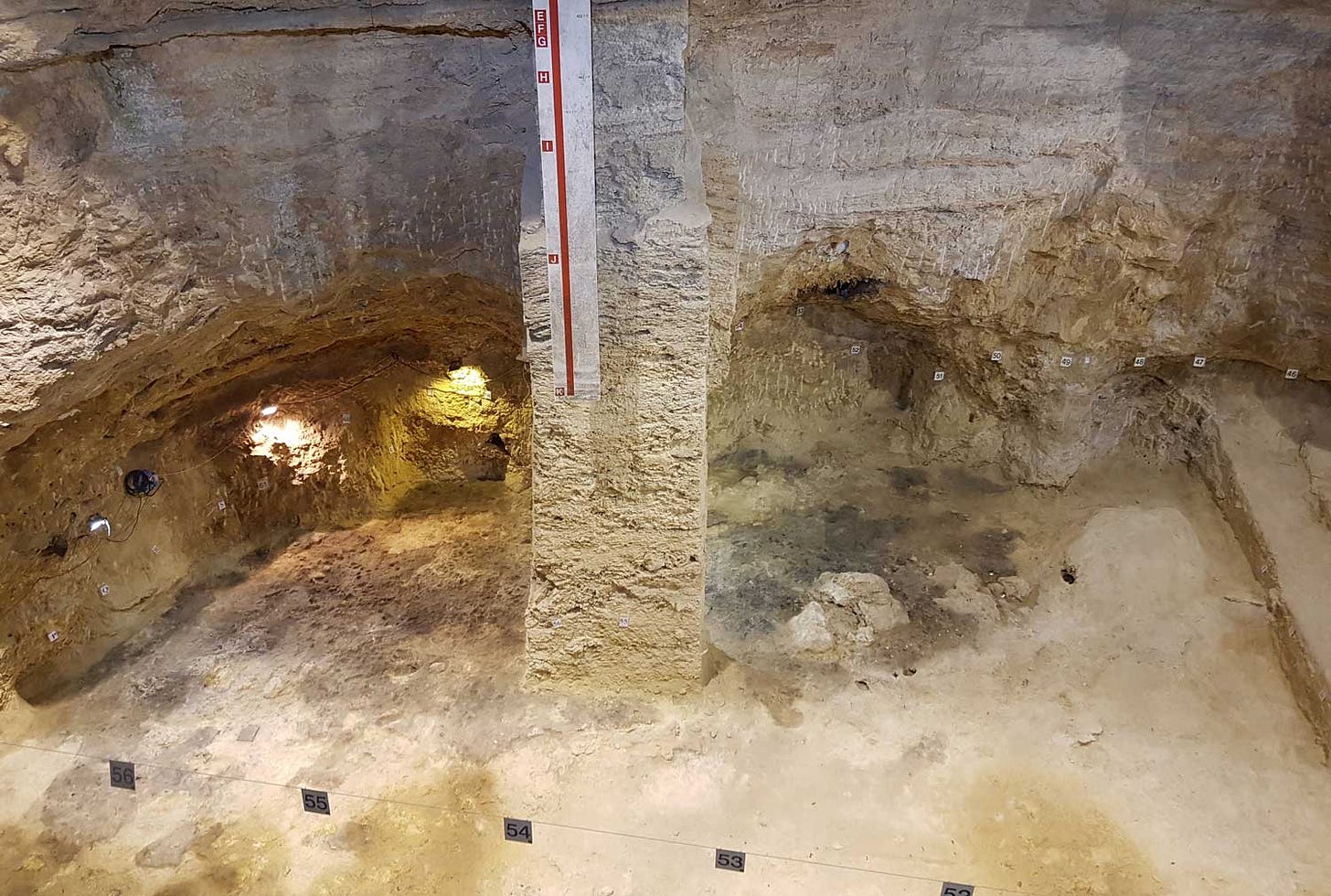 A rock wall with a column of remaining sediment at the center of image surrounded by excavation area