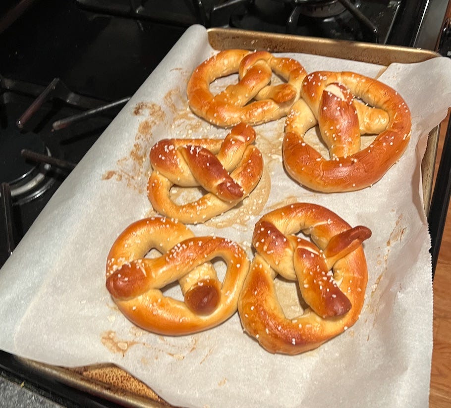 a baking sheet with five fresh hot pretzels on it