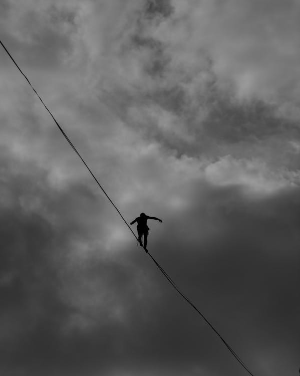 Free A silhouette of a person balancing on a tightrope against a dramatic, cloudy sky. Stock Photo Free A silhouette of a person balancing on a tightrope against a dramatic, cloudy sky. Stock Photo