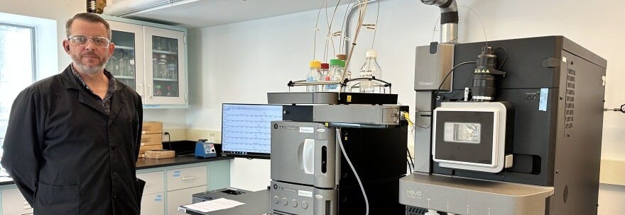 Barnstable County Water Quality Laboratory chemist Andrew Barker stands next to the lab's new, state-of-the-art equipment for PFAS analysis. It's called a liquid chromatography mass spectrometer, and Barker calls it "the Ferrari of instruments." Barker was a critical part of the lab's certification process, according to a county spokesperson. If you submit a sample to the county lab for PFAS analysis, Barker is the one who will analyze it.