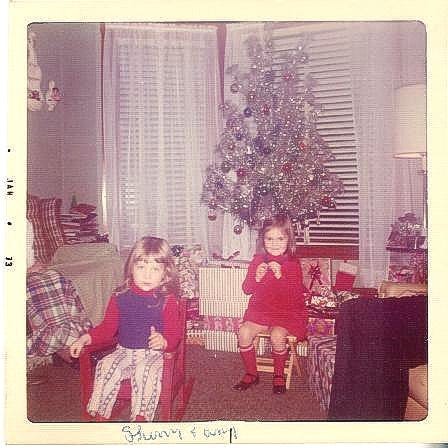 an old photo of me as a toddler wearing 70s clothes and sitting in a little red rocking chair next to my cousin, both of us posed in front of a classic silver 1970s Christmas tree