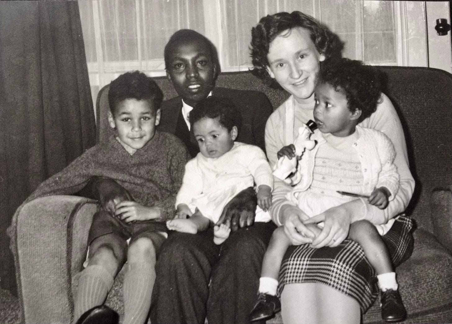 professional photo of Black man, White woman and kids aged around 8, 2 and infant --seated on a sofa