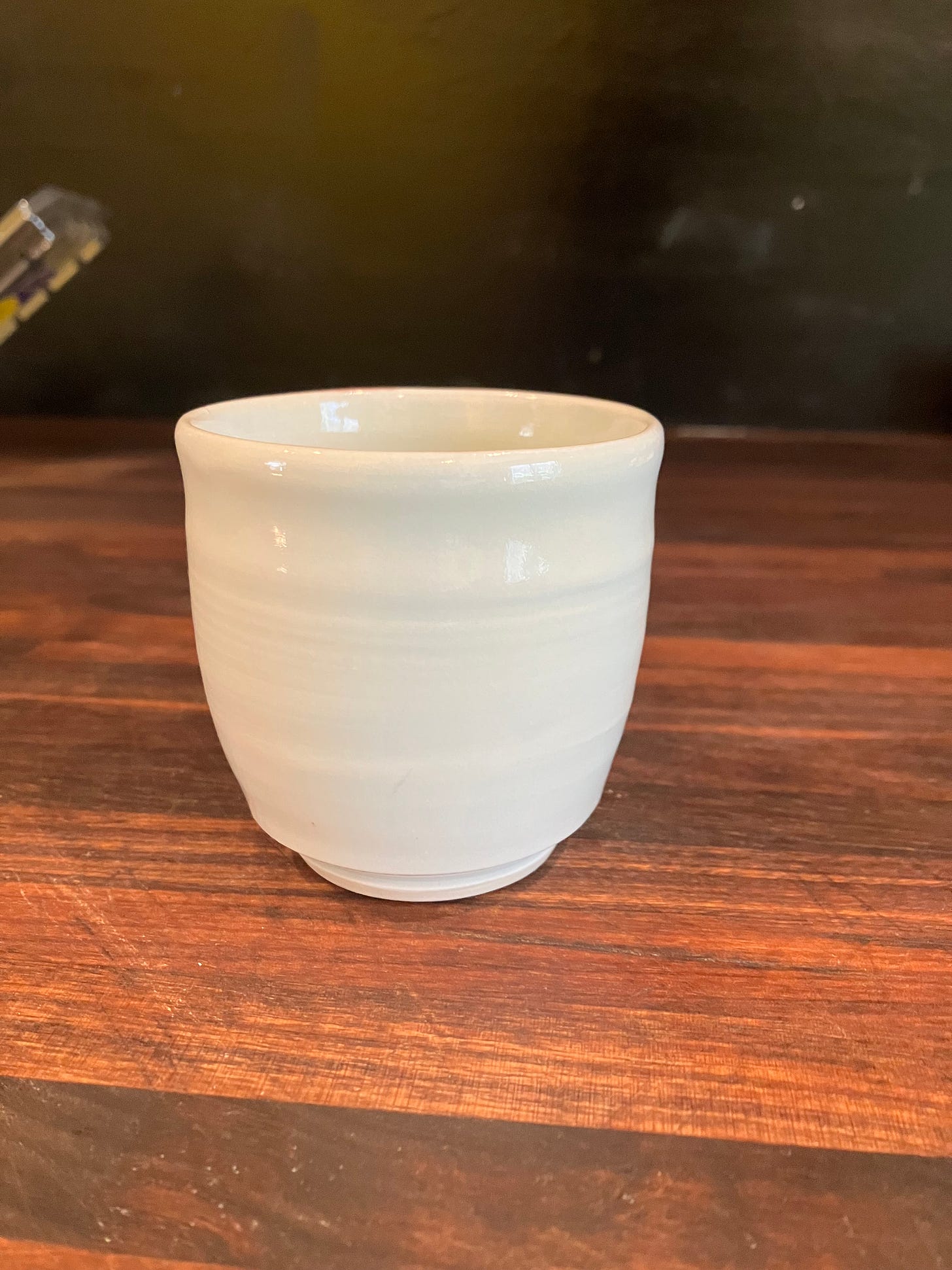 light blue celadon porcelain demitasse cup on a walnut butcher block with a black background