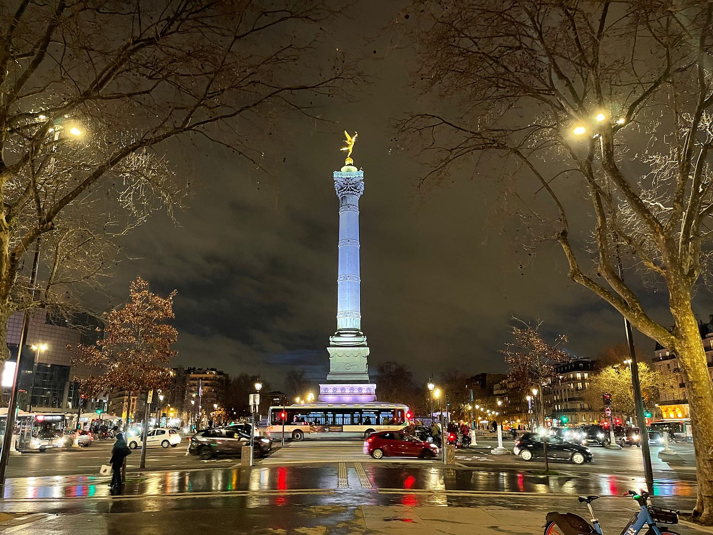 the central column of the square against a dark sky, many reflecting lights on the dark pavement