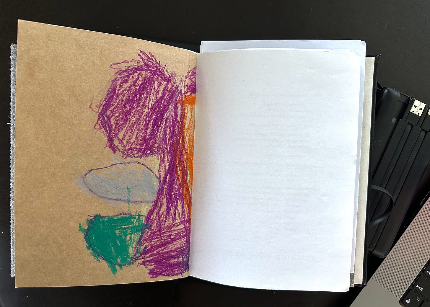 An open notebook on a dark background, with a child’s crayon drawing on brown paper on the left hand page.