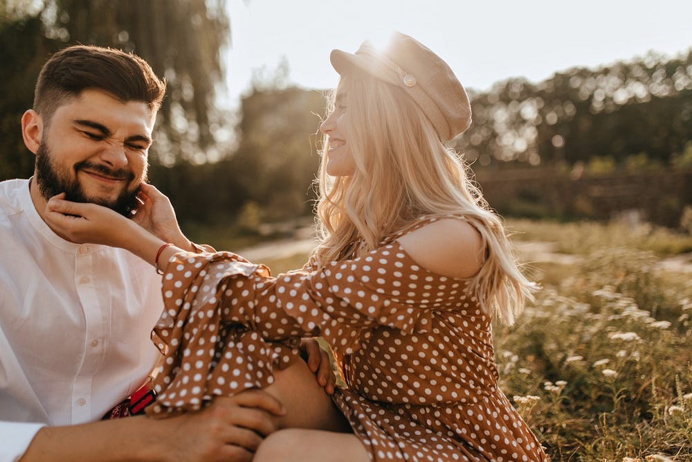 Smiling woman tickles a bearded man in an outdoor setting with sunlight on the background. Smiling woman tickles a bearded man in an outdoor setting with sunlight on the background.
