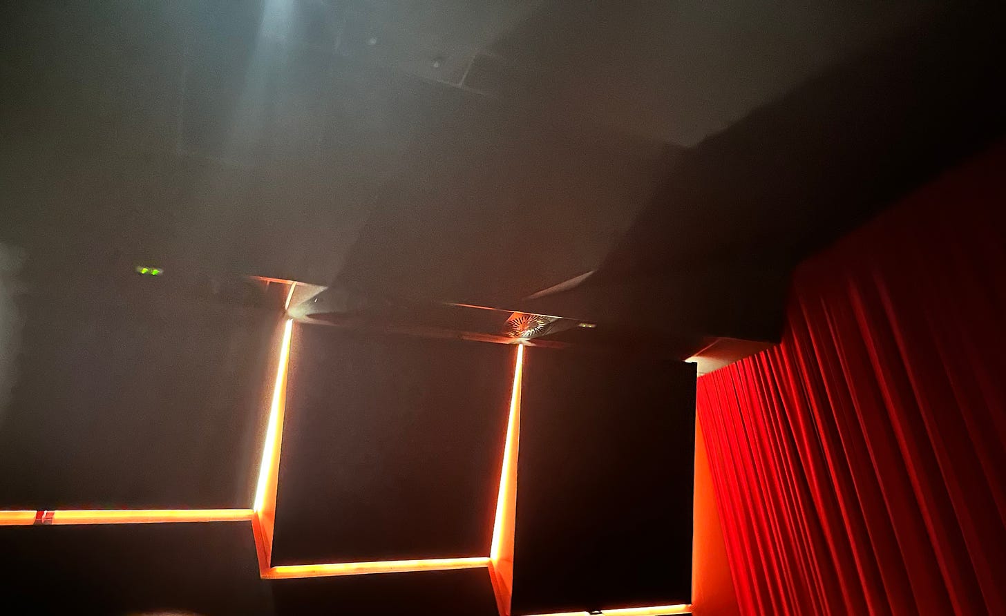 An image of the interior of a movie theater, with dramatic lightining and an ominous curtain 