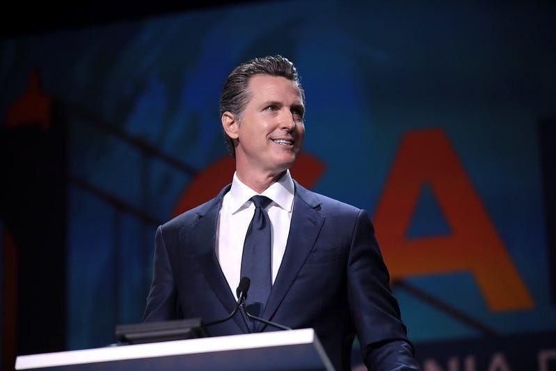 A smiling Gavin Newsom stands at a podium 