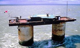 An old photo depicts two men stand atop a tall industrial platform in the middle of the sea