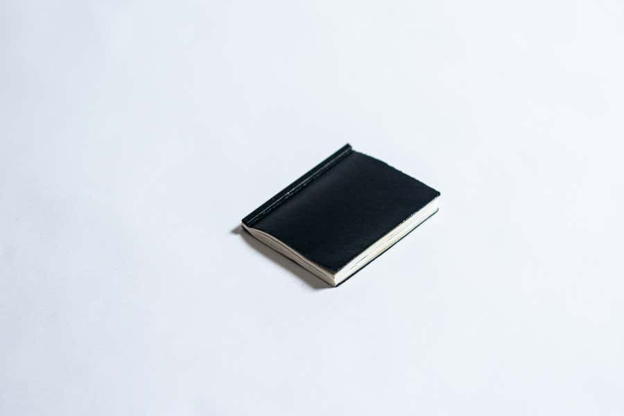 A small, black leather bound notebook laying down on a field of white.