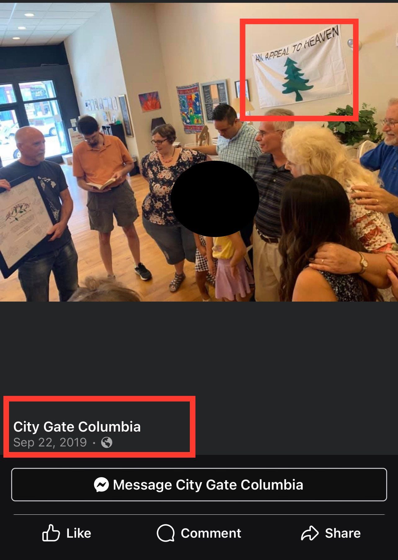 A screen capture image from the Facebook account of City Gate Columbia. People are laying hands on each other in prayer. An Appeal to Heaven flag hangs from the wall behind them.