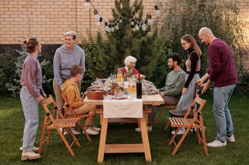 Free Happy family members talking and sitting down to eat tasty food at big wooden table in backyard in daytime Stock Photo