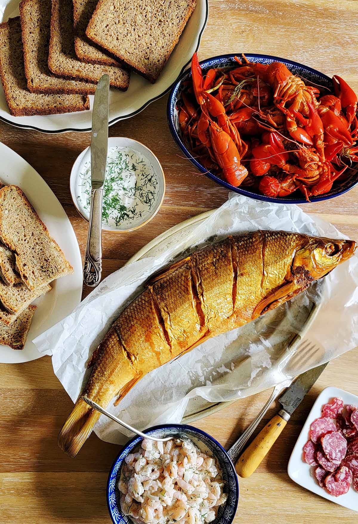 A spread of rye bread, smoked fish, crayfish, shrimp salad and salami on a table. 