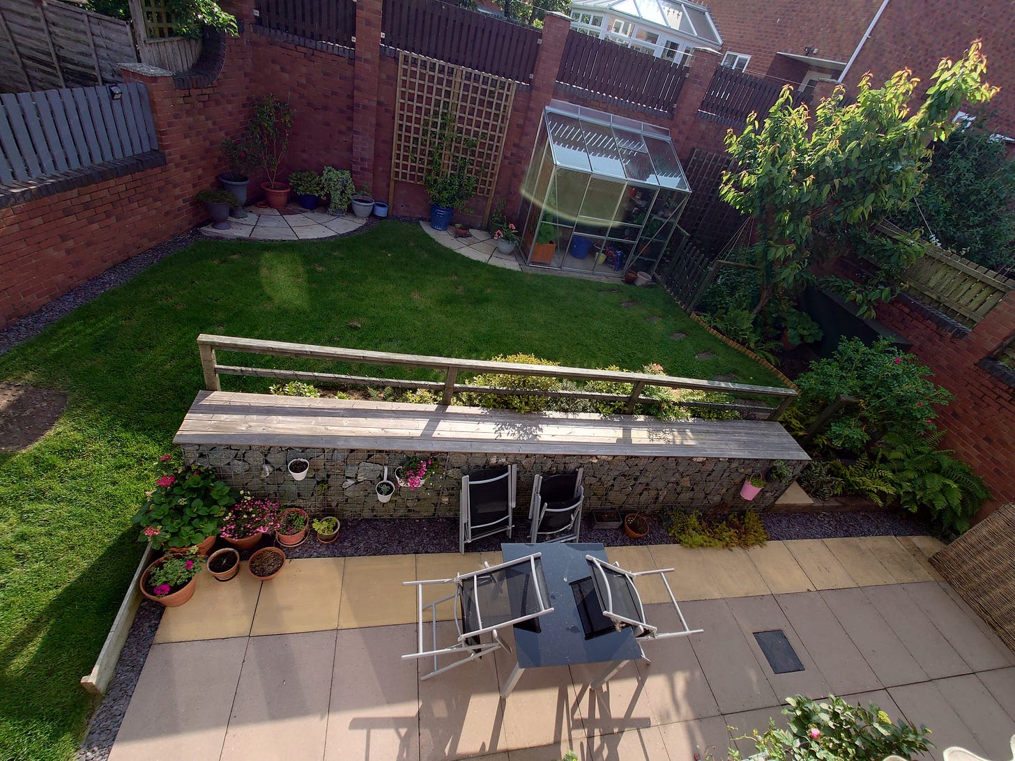 Photo of upper back garden in early morning, including patio, gabion wall, fernery, veggie patch, greenhouse, stone circles and lawn