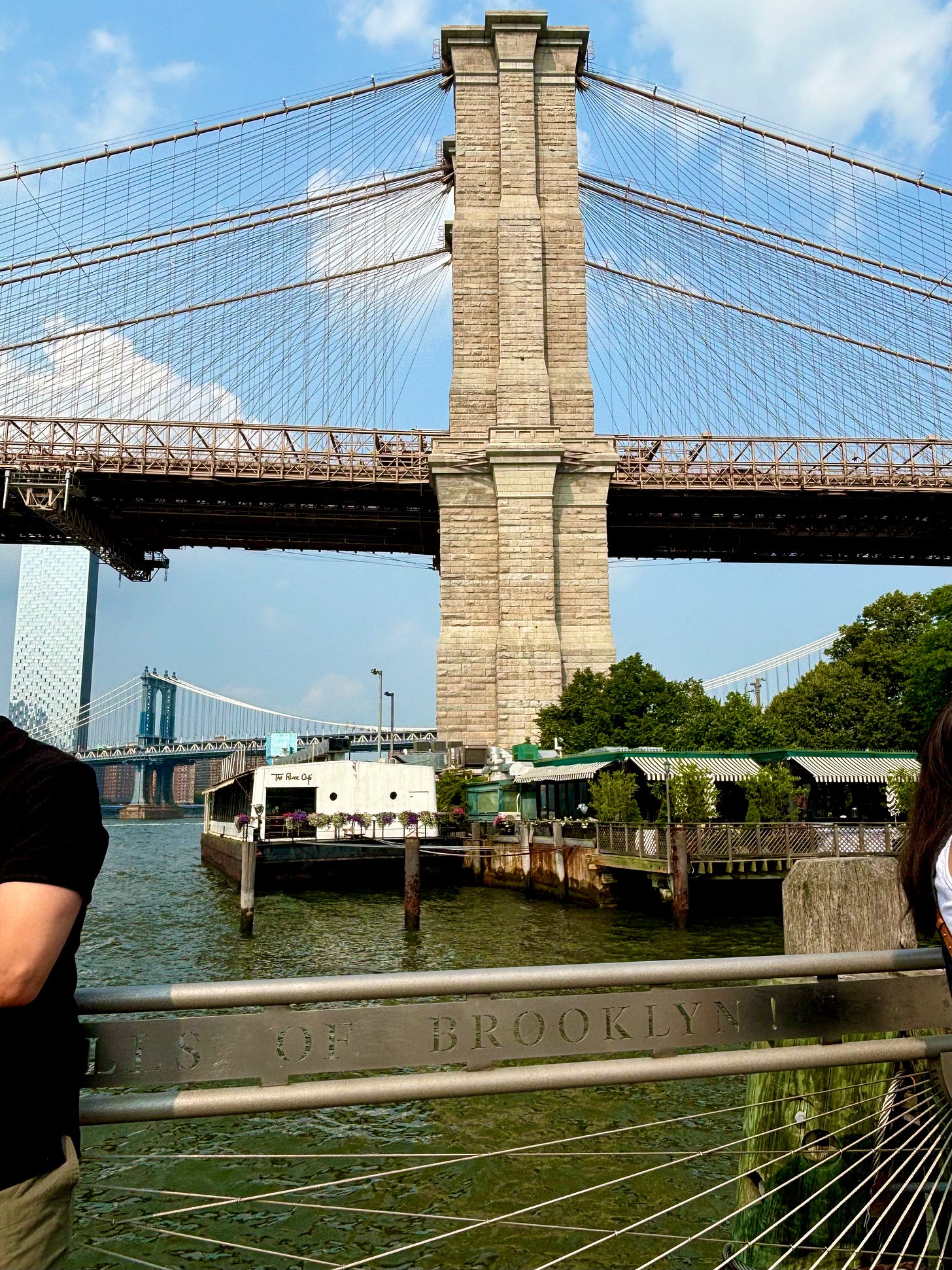 The Brooklyn Bridge from Pier 1. Two people are leaning out of the frame that seems to be shouting "BROOKLYN!" at you. The entire rail is engraved with Walt Whitman's "Crossing Brooklyn Ferry" and this is the final word.