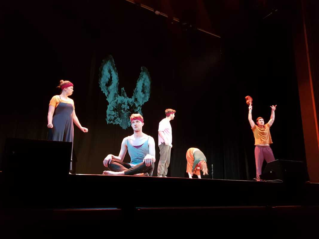 Actors perform on a stage, with a brain/rabbit screen on the background